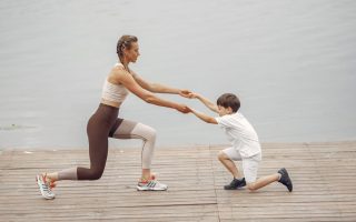 A woman and a boy exercise together on a wooden deck by the lake, promoting healthy lifestyle.