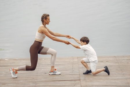 A woman and a boy exercise together on a wooden deck by the lake, promoting healthy lifestyle.